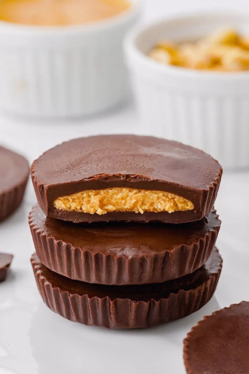 A stack of three homemade chocolate peanut butter cups, the top one bitten to show the filling