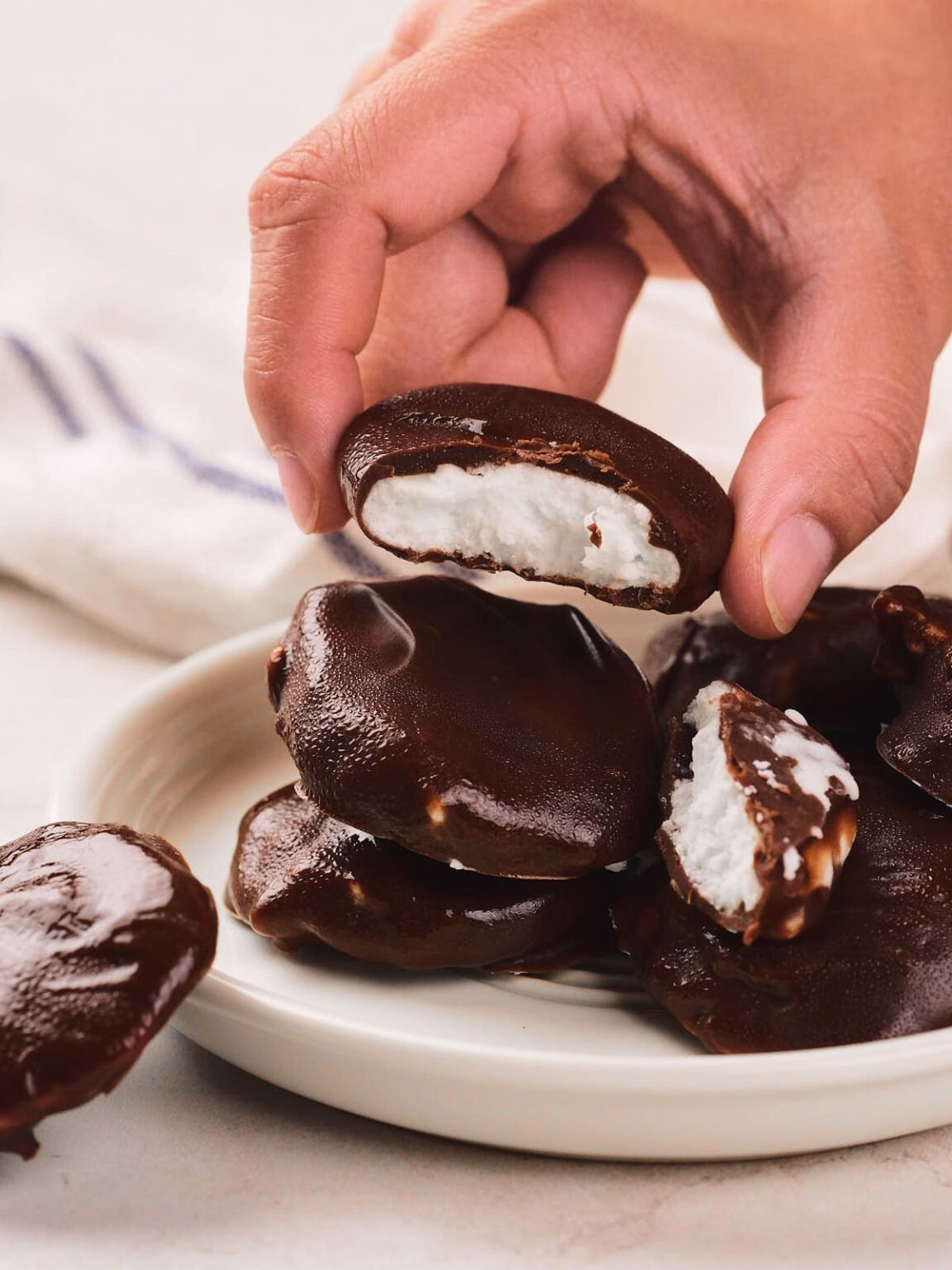 A hand lifting a bitten chocolate-covered peppermint patty from a plate of patties, showing the white filling